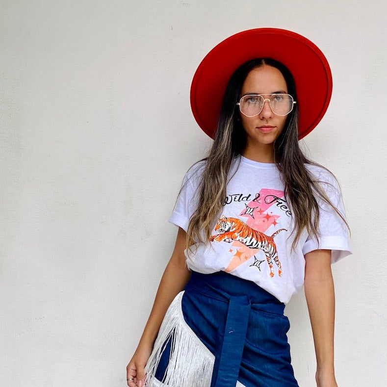 Camiseta blanca de mujer con diseño dinámico de tigre de Bengala saltando un rayo rosa y la frase Wild and Free. Libera tu espíritu y vive con pasión