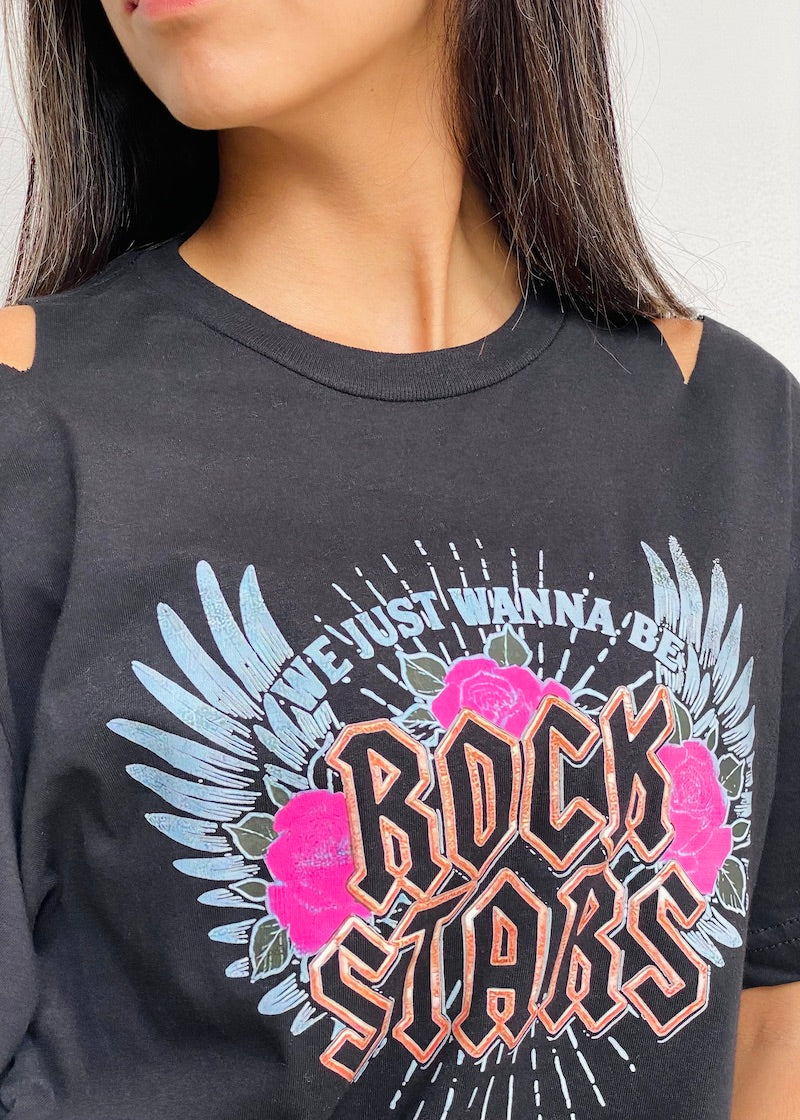 Camiseta negra de mujer con la frase "We just wanna be Rock Stars" en rosa, acompañada de alas celestes y rosas. Descubre más en Free Spirit.